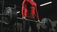 Muž zvedá činku v posilovně během silového tréninku, fitness a kulturistika